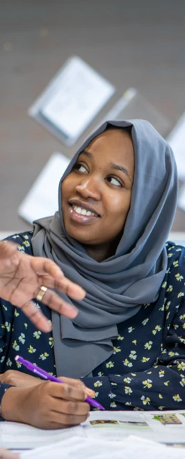 A teacher leans in to engage with students in a classroom, offering guidance while a female student in a hijab smiles and listens attentively. A teacher leans in to engage with students in a classroom, offering guidance while a female student in a hijab smiles and listens attentively.